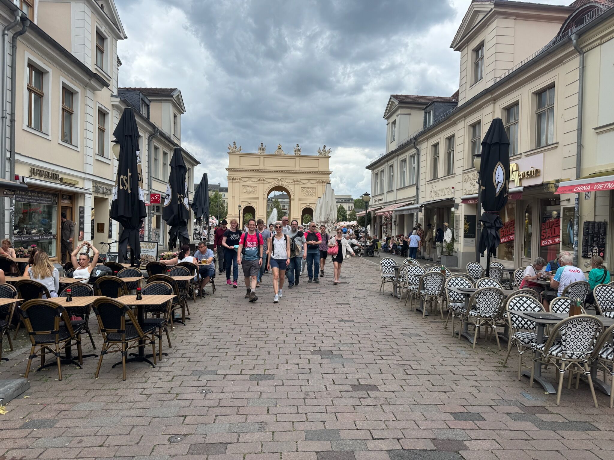 Gruppe von Menschen läuft gemeinsam zu Fuß durch die Potsdamer Innenstadt, im Vordergrund das historische Berliner Tor.