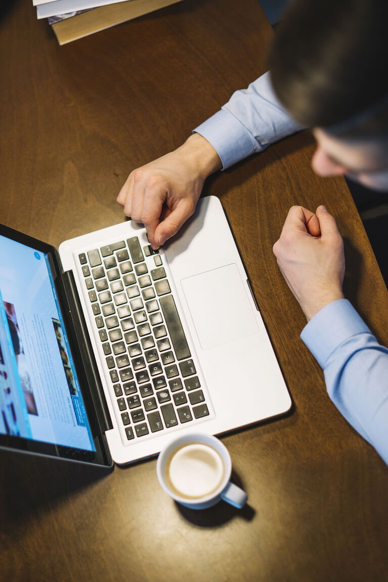 Mann am Laptop mit Kaffeetasse nutzt das Self-Service-Kundenportal früh am Morgen vor der Arbeit
