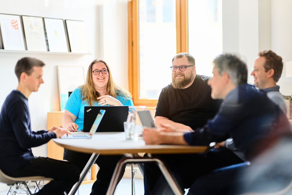 Teammeeting bei escape mit fünf Personen am Tisch und Laptop
