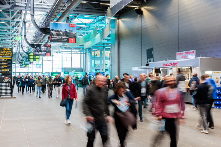 Teilnehmer einer Fachkonferenz bewegen sich durch eine Messehalle – typischer Anwendungsfall für digitale Konferenzplattformen und Event-Management.