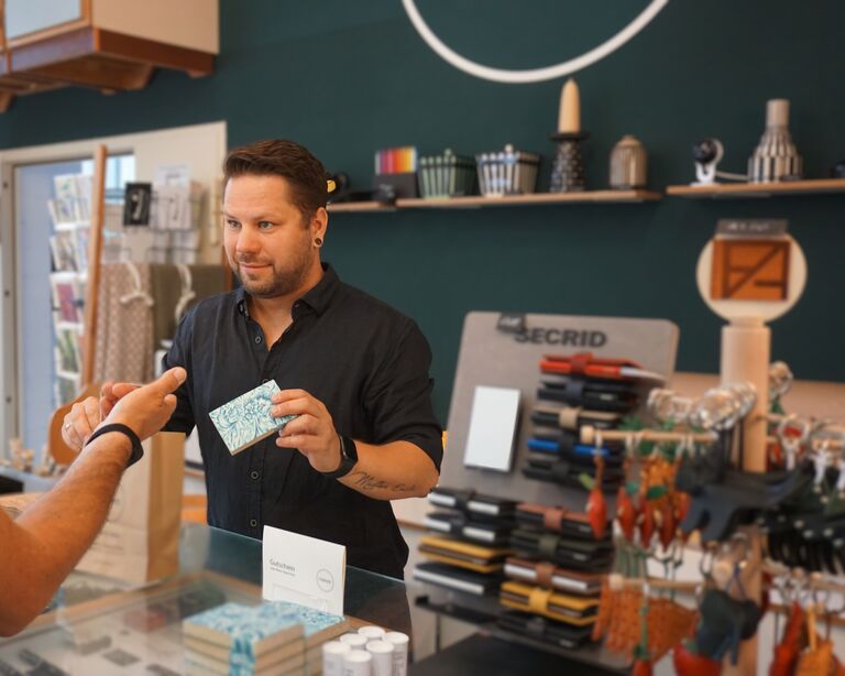 Marcel, Store Manager bei FORMOST, reicht ein verpacktes Produkt über die Ladentheke an einen Kunden