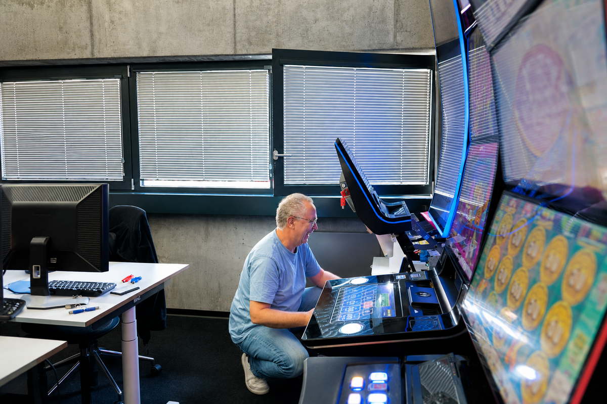 Tests an den Automaten Mann kniet vor beleuchtetem Spielautomaten und testet das Touch-Display
