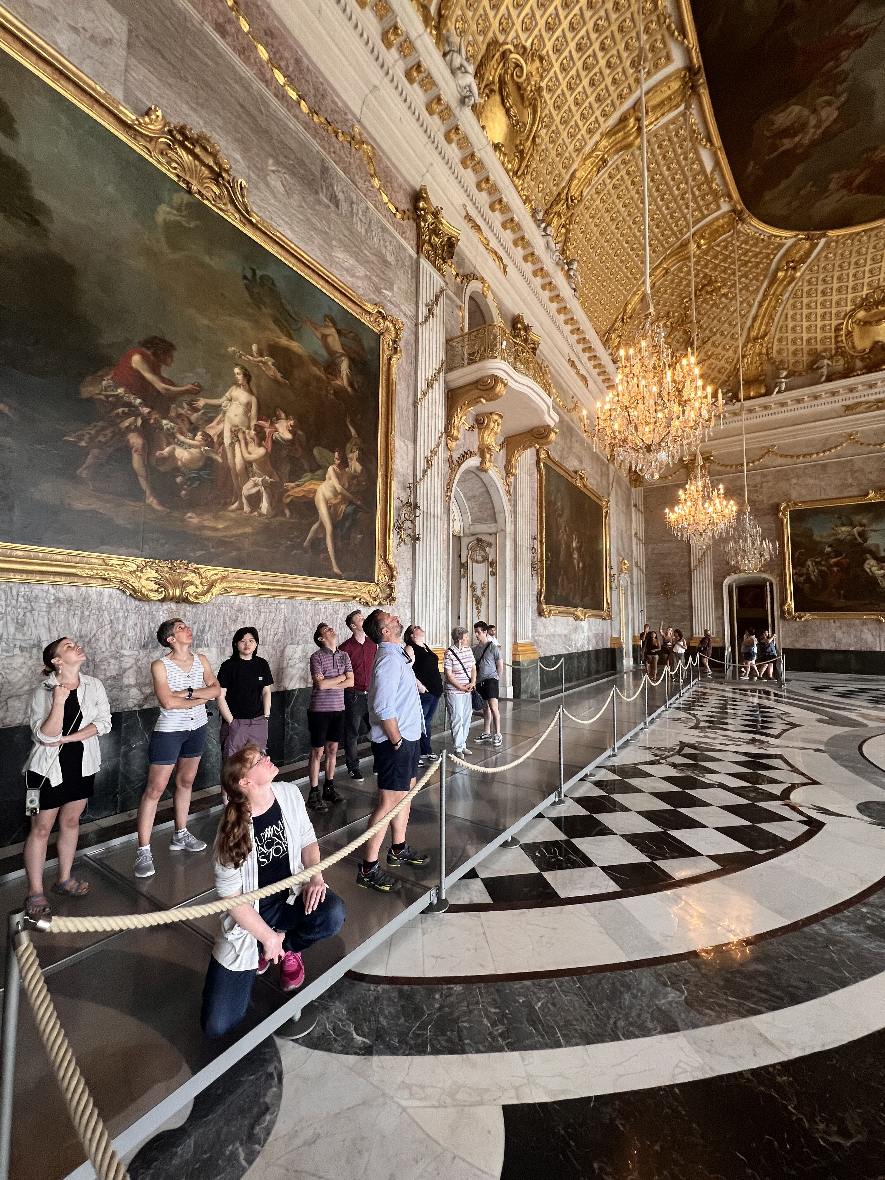 Mehrere Kolleginnen und Kollegen stehen im Marmorsaal des Neuen Palais und blicken fasziniert nach oben auf die reich verzierte Decke mit Stuck und Fresken.