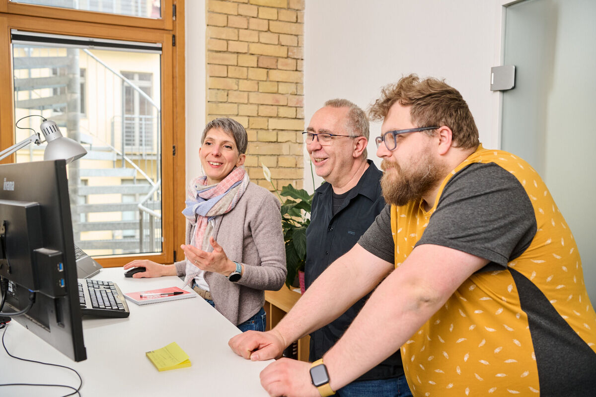 Ein Team aus Kolleg:innen einer Digitalagentur arbeitet gemeinsam an einem Monitor, bespricht Ideen und überprüft technische Lösungen.